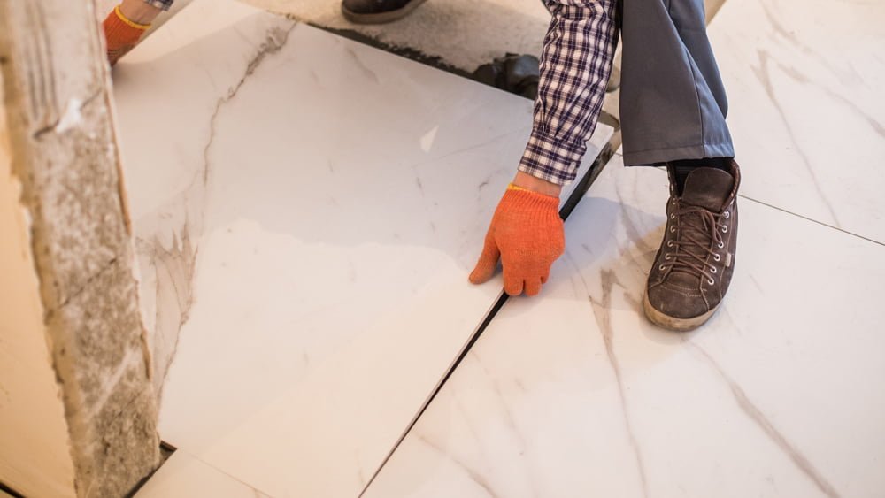 Professionnel ajustant méticuleusement un carreau de marbre blanc veiné de gris.