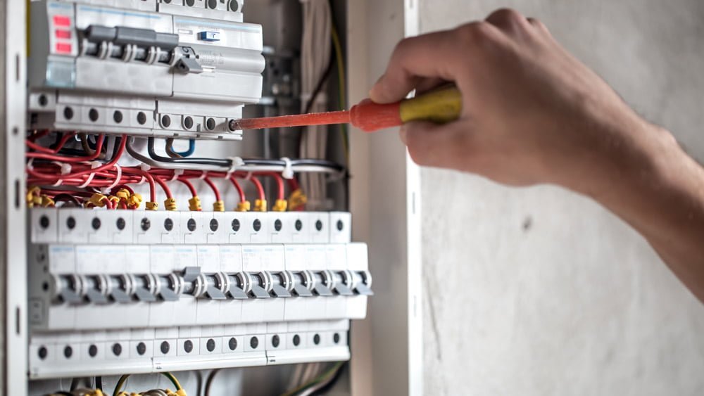 Technicien effectuant la maintenance sur un panneau électrique avec des disjoncteurs.