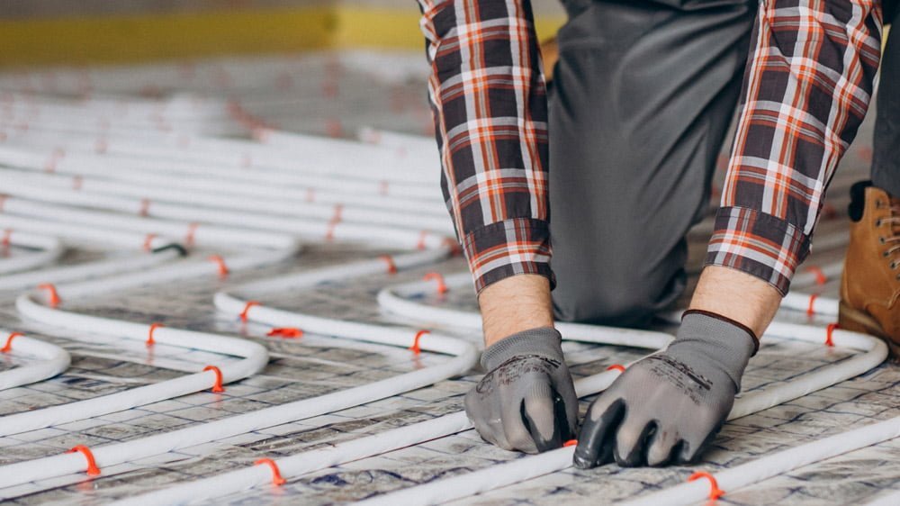 Installation d'un système de chauffage au sol par une personne en tenue de travail pratique.